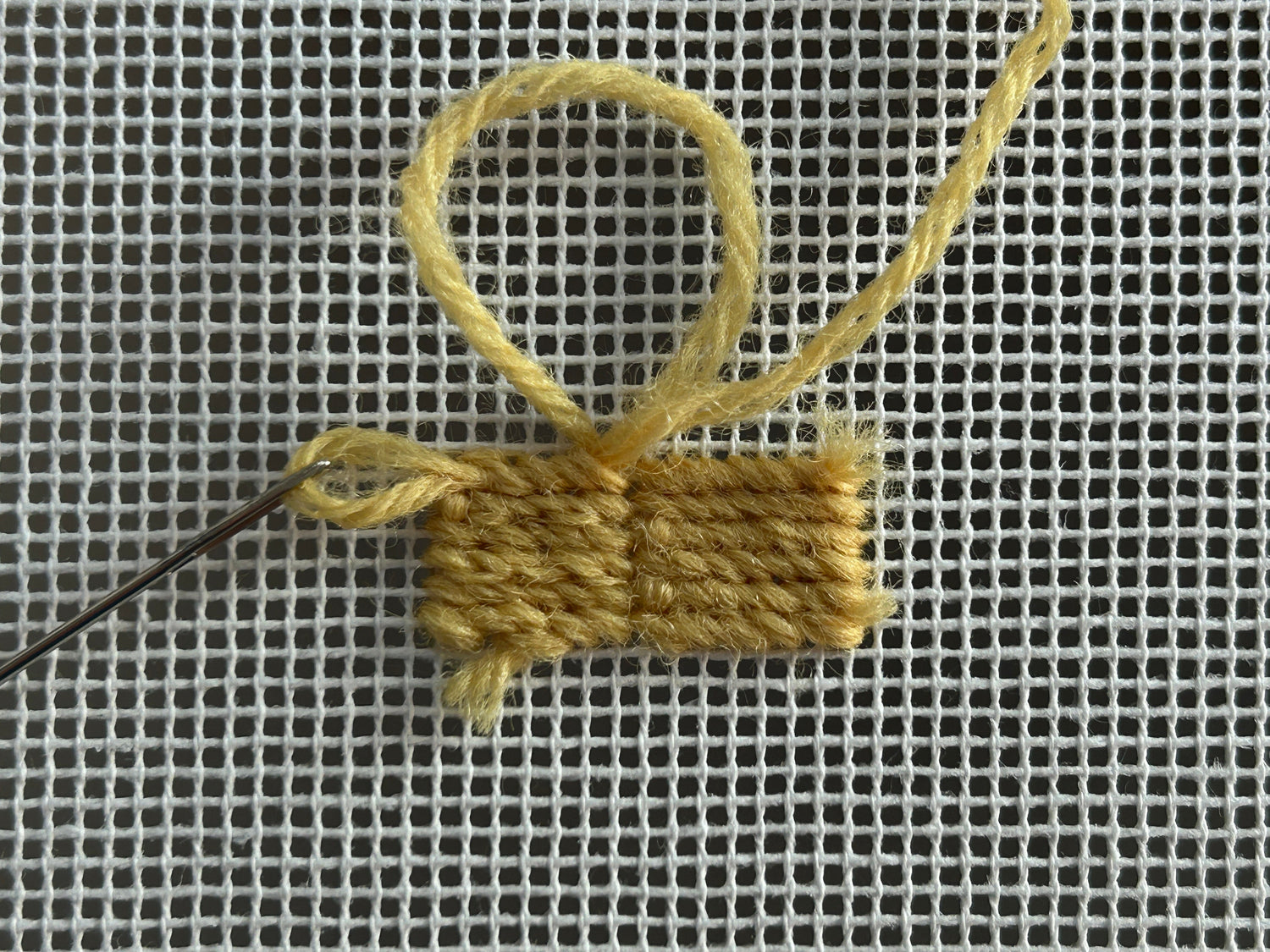 How to finish off a piece of yarn by threading the yarn through the back of stitches at the back of the needlepoint canvas